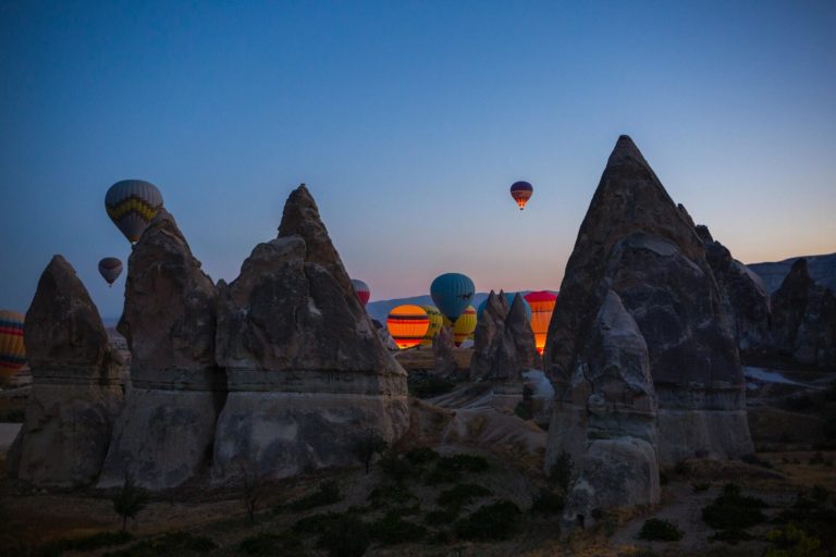 A lone hot air balloon rises from a group among mountains at sunset.