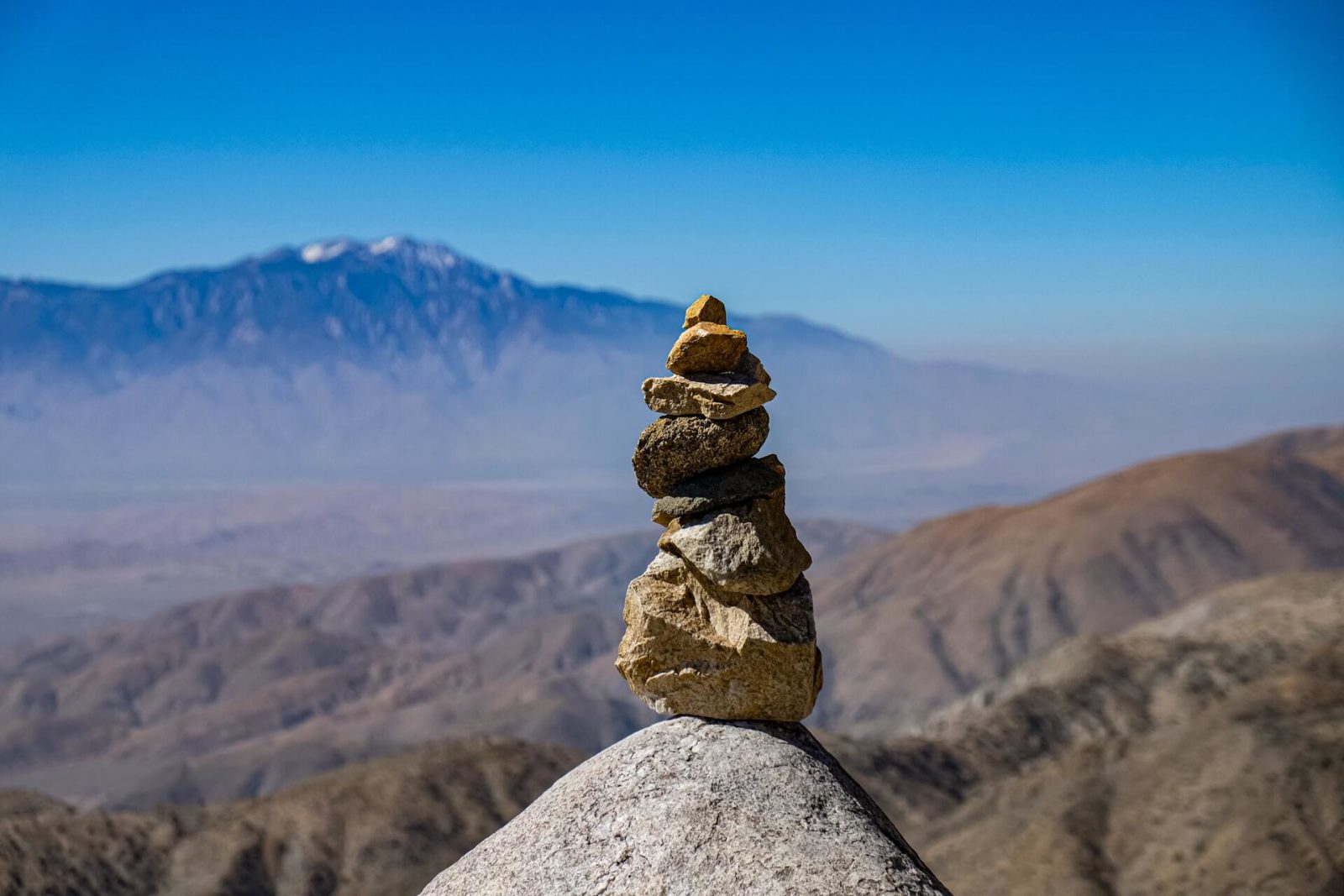 A stack of rocks on a stone precipice with a mountain vista in the background.