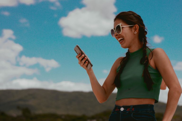 Woman in green tank top holding a smartphone outdoors