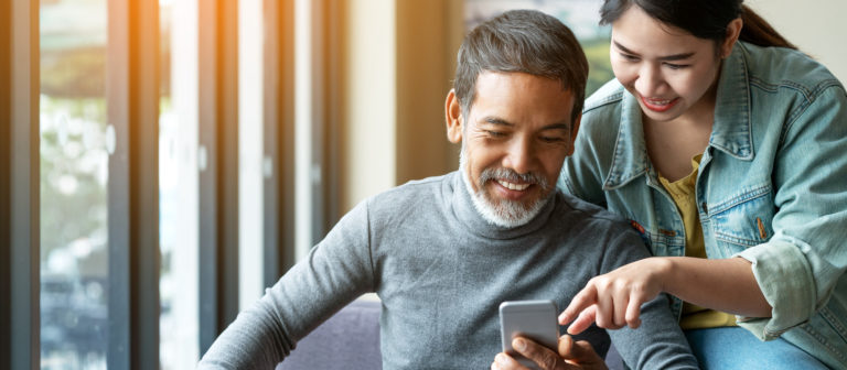 A father and daughter smile as they engage with a brand on their smartphone.