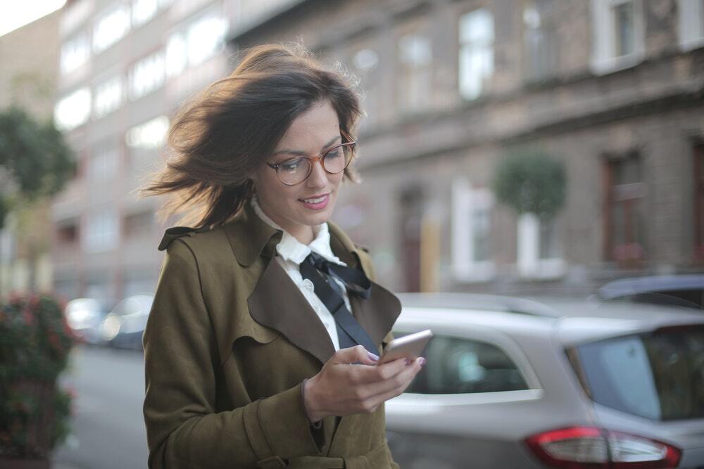 Young female professional using a messaging app on her smartphone while taking a walk outside.