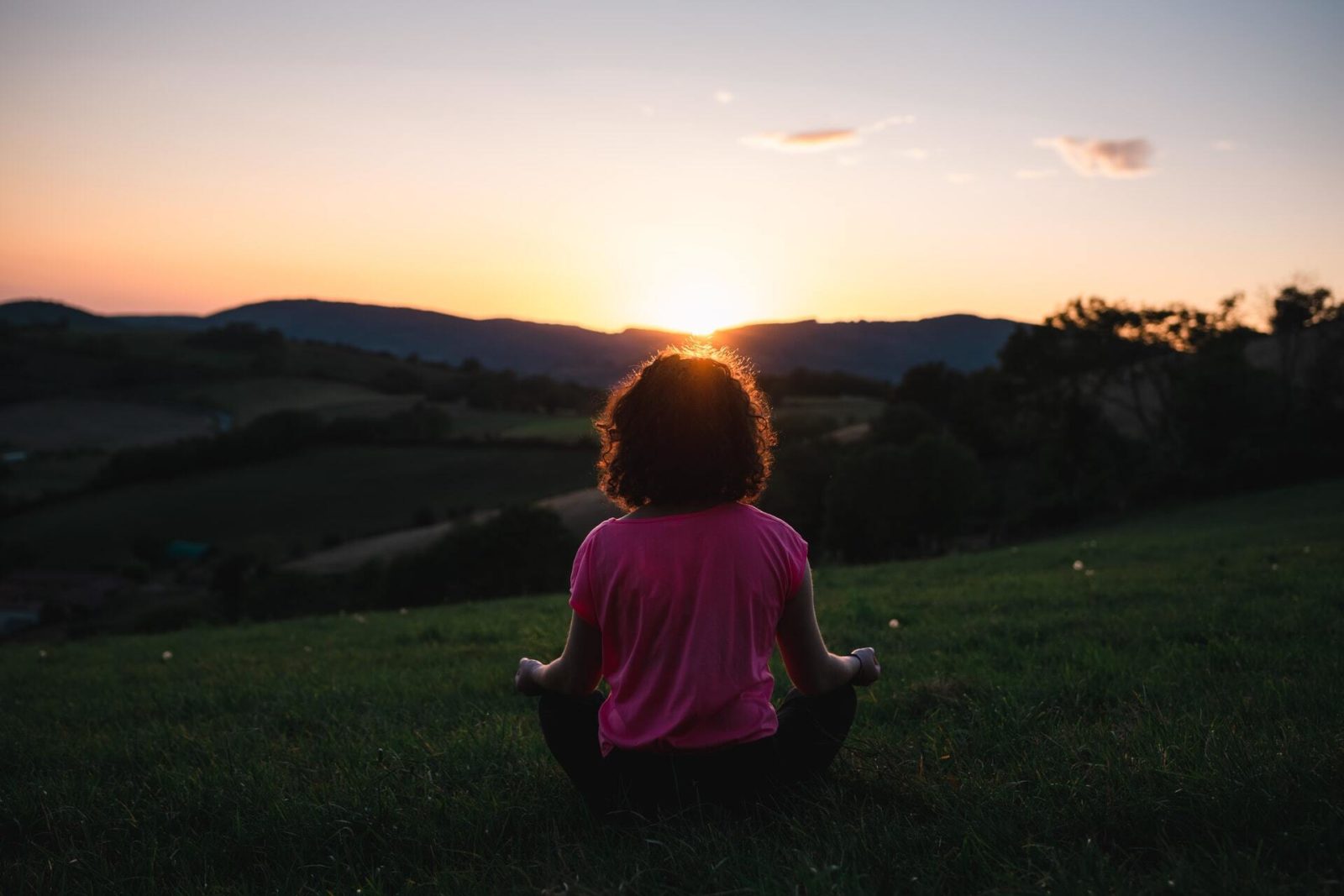 A person meditating on grass at sunset.