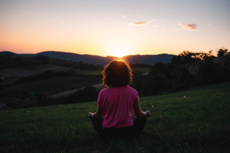 A person meditating on grass at sunset.