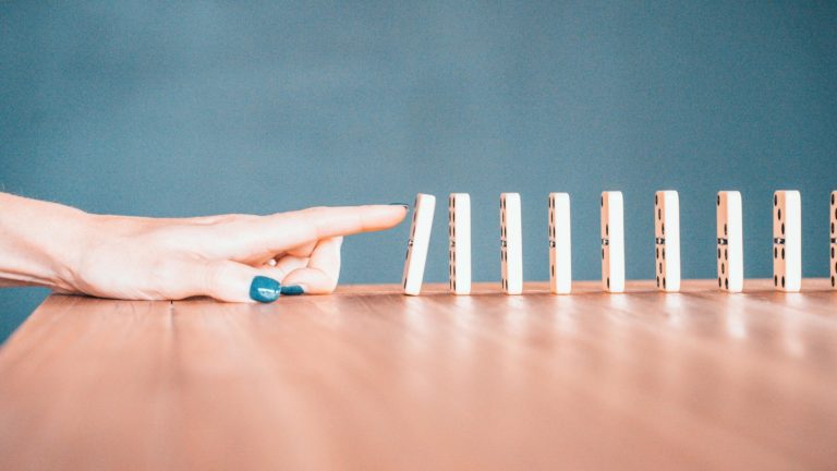 A finger pushing down a line of dominoes.